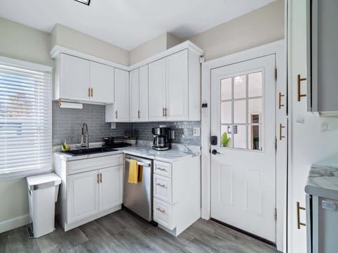 - Kitchen corner with dishwasher and sink station ready   - White cabinets with brass pulls add stylish contrast   - Access to backyard makes meal prep fresh and convenient  