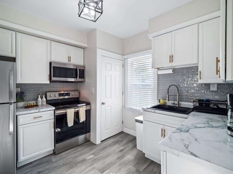 - Modern kitchen with stainless steel stove and microwave   - White cabinetry paired with sleek subway tile backsplash   - Bright window light highlights the marble-look counters  