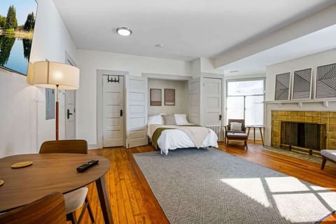 Bright open studio w/ cozy bed, fireplace lounge & dining table set on warm hardwood floors
