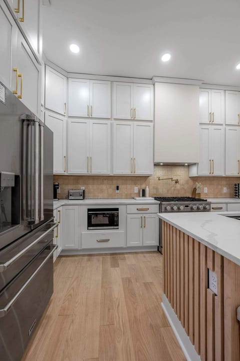 Modern kitchen featuring crisp white cabinets, stainless steel appliances, and a spacious island. Ideal for cooking and entertaining, enhanced by elegant lighting and a stylish bar cart.