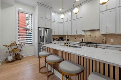 Modern kitchen with sleek white cabinetry, stainless steel appliances, and a large island with seating. Perfect for cooking and gathering, featuring stylish lighting and a cozy bar cart by the window.