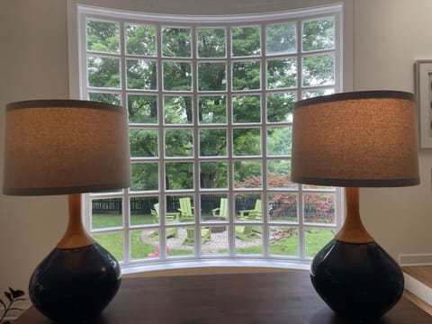 Enjoy a charming view from the living room, framed by stylish lamps, offering a glimpse of the firepit and garden outside in Saugatuck