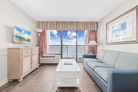 Direct Oceanfront living room with balcony overlooking Myrtle Beach, the Atlantic Ocean, and the Monterey Bay Suites Outdoor Pools.  This stylish living room is fully equipped with a Smart TV, full-sized queen sofa sleeper, and dining room.