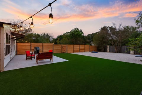 This cozy, modern backyard guest house features a sleek white exterior, large windows, and a welcoming patio area with vibrant red outdoor seating.