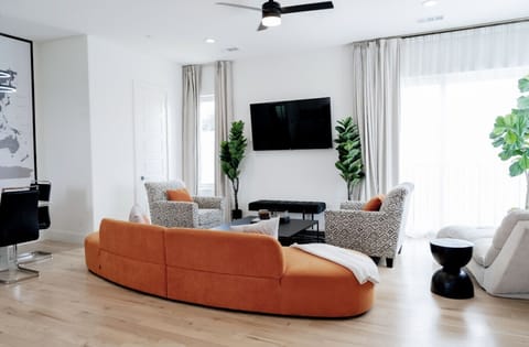 Sunlit living room with soaring ceilings, modern orange lounge seating, and an open-concept layout designed for comfort and connection.