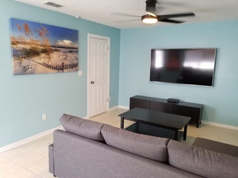 Bright living room with large TV, comfortable seating, and vibrant beach artwork.
