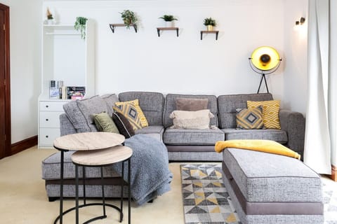 Bright living room with generous sectional seating and contemporary furniture. Large windows provide natural light. Includes a geometric-patterned coffee table and built-in storage.
