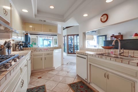 Open layout with tiled countertops, dual sink, and serving window overlooking the living area