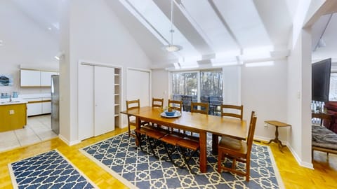 A dining area with a wooden table set for eight overlooking a deck and lake through sliding glass doors.