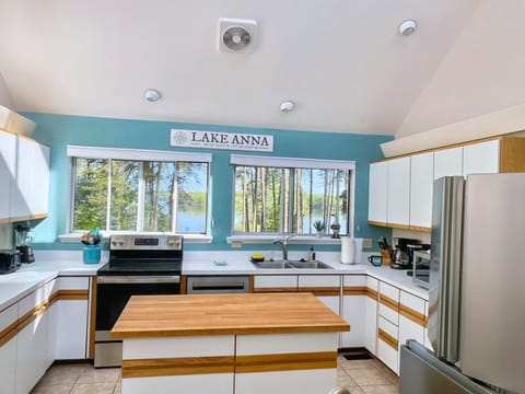 A spacious kitchen with a large island, barstools, and modern appliances with scenic lake views through the window.