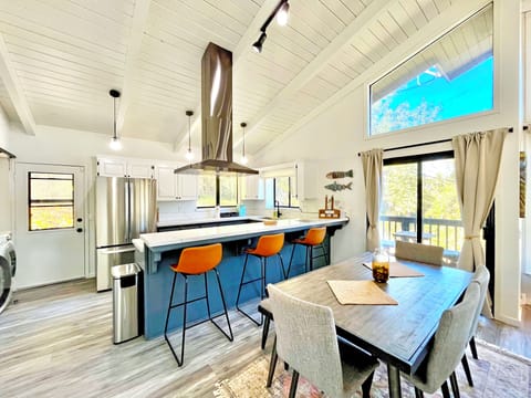 Bright kitchen/dining area with bar seating, vaulted ceilings, and forest views.