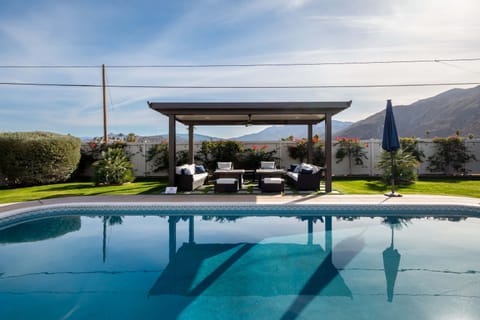 Sunlit pool with pergola lounge, lush lawn, and sweeping mountain backdrop — the kind of backyard that fills up fast after check-in