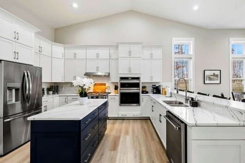 Bright open-concept kitchen and dining area with white cabinets, a navy island, and large windows providing natural light and scenic views.