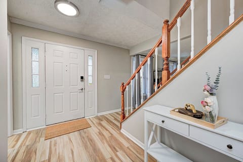 This is an entryway with a white front door. The space has light wood-style flooring, neutral walls, and a staircase with a wooden handrail and white spindles.  A small white console table naturally blends in with the other decor.