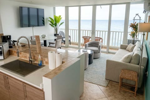Modern oceanfront living space with open kitchen and floor-to-ceiling windows — enjoy stunning sea views from every corner of this bright, stylish retreat.