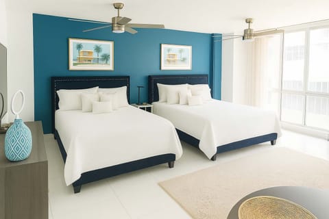 Spacious and stylish bedroom featuring two plush beds, chic coastal decor, and natural lighting — ideal for families or friends seeking comfort just steps from the beach.