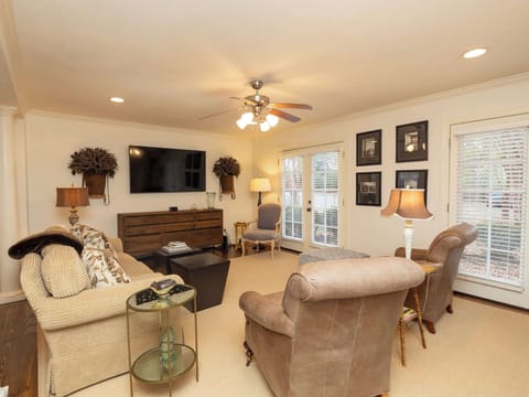 A warm and inviting living room featuring cozy armchairs, a large sofa, and a wall-mounted TV under a classic ceiling fan.