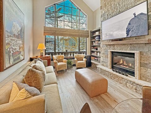 Unwind in the cozy living room with plush seating, a stone fireplace, massive smart TV, and mountain views through soaring windows, perfect après-ski comfort in Arrowhead Village.
