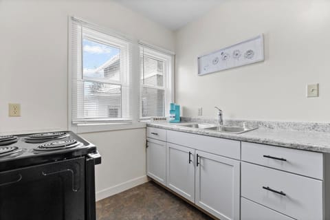 Modern full kitchen featuring a sleek sink with faucet, stylish cabinets, elegant granite countertops, a stove, and large windows allowing natural light—combining functionality and contemporary design for an inviting cooking space