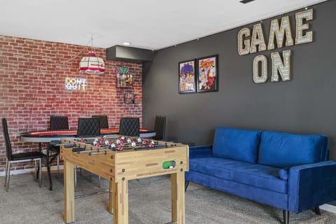 Lower level game room with a 6 seat poker table, board games, foosball, Pac-Man arcade game, 50" smart TV, and bar top with 2 barstools.