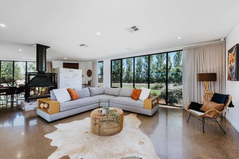 The spacious and stylish living area features a modern L-shaped sofa, warm wood accents, and large windows offering serene garden views.