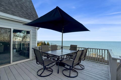 A deck with a dining set and umbrella overlooking calm waters and a clear blue sky.