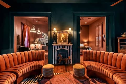 Original fireplace mantels, vintage artwork, and tall windows dressed in black drapery create a moody, sophisticated New Orleans vibe. The double doors on the right is the entry to the first bedroom.