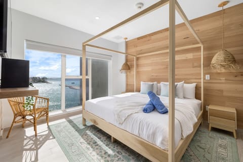 Step into your serene coastal retreat where warm wood tones meet stunning ocean views. Unwind in your canopy bed with crisp linens, soaking in breathtaking water vistas through floor-to-ceiling windows.
