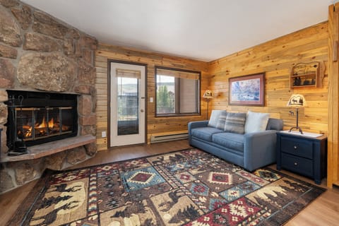 Cozy up by the crackling stone fireplace in your rustic living room, where warm wood walls and mountain charm create the perfect retreat.