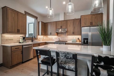 - Modern kitchen design with under cabinet lighting and tile backsplash
- Island seating for two provides a casual spot for meals or conversation
- Stainless steel fridge and gas range complete the functional space