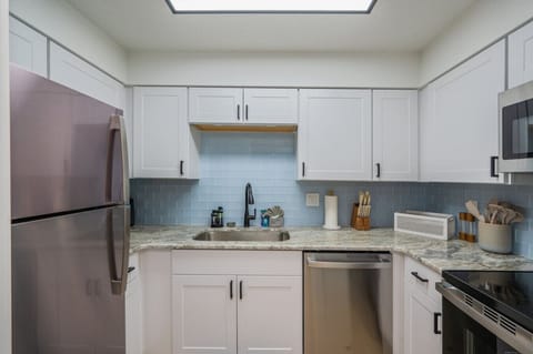 Fully equipped kitchen with fridge, sink, and modern white cabinets.