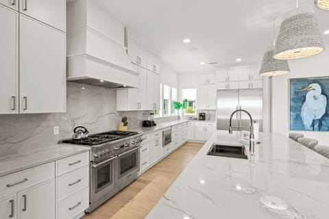 You'll love preparing meals in this elegant white kitchen with marble countertops, stainless steel appliances, and stylish pendant lighting.