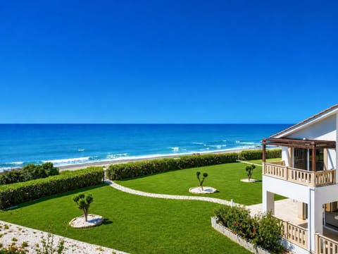 An elevated, scenic view from a coastal property looking out over a beautifully manicured lawn toward the open sea.
