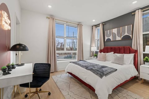 Elegant and inviting bedroom with a luxurious red upholstered bed, modern desk setup, large windows for natural light, and sophisticated décor, ideal for comfort and productivity.