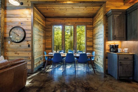 A cozy breakfast nook with large windows and forest views offers the perfect spot for morning coffee. Featuring modern rustic design, this dining space adds warmth to a vacation rental, making every meal a relaxing nature retreat moment.
