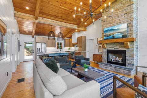 Cozy meets modern in this open-concept living area with a stone fireplace, vaulted wood ceilings, and stylish lighting.
