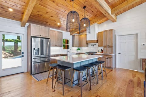 Modern kitchen with high-end stainless steel appliances, granite countertops, and wood cabinetry. Features a central island with seating for five, pendant lighting, and exposed wood beams.