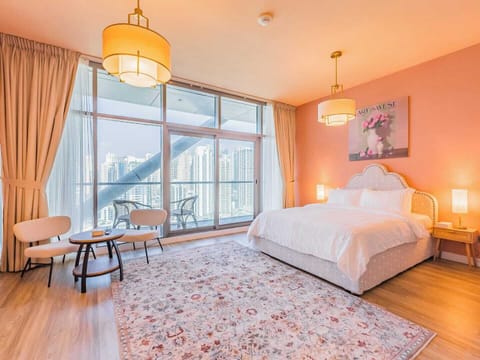Elegant and airy bedroom with a king-size bed, soft peach walls, and chic lighting. Features floor-to-ceiling windows, a private balcony with stunning city views, and cozy seating—perfect for a stylish, relaxing stay.
