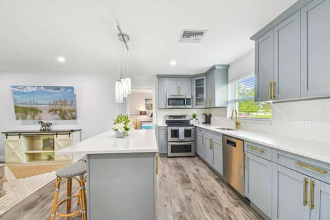 Modern luxury kitchen in Florida vacation rental with grey custom cabinets, gold hardware, and stainless steel appliances. Open-concept design with quartz countertops, coastal artwork, and designer lighting in Largo Florida near Indian Rocks beach