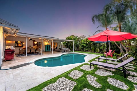 Captured at dusk, this photo reveals the enchanting ambiance of the pool area with warm lighting illuminating the space. The red umbrella and cozy seating area invite relaxation as the sun sets, creating a perfect evening retreat.