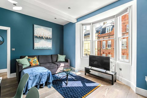 Bright and modern living room with a cozy sofa, smart TV, and large bay window offering plenty of natural light and charming street views
