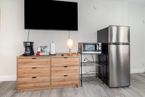 Enjoy the comforts of home with a sleek stainless steel refrigerator, microwave, and coffee station. A large smart TV and storage options complete this convenient and functional setup.