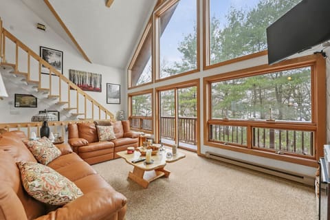 A bright and spacious living area with a large leather sectional, and floor-to-ceiling windows overlooking the trees.