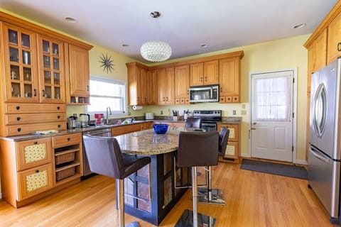 Open-concept kitchen and dining space designed for entertaining, featuring an eat-in island, modern lighting, wooden cupboards, full stove range, dishwasher, and microwave.