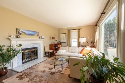 Cozy, sun-filled living room featuring a fireplace, plush sectional sofa, and expansive windows offering serene views of the outdoors.