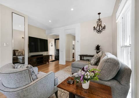 A welcoming living area featuring a mounted TV, elegant full-length mirror, and a timeless chandelier, blending modern comfort with vintage charm.