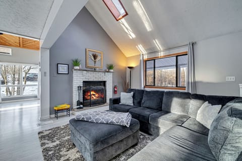 Spacious and inviting living area with a cozy fireplace, vaulted ceilings, and large windows offering natural light and serene views – perfect for family gatherings or relaxing by the fire.