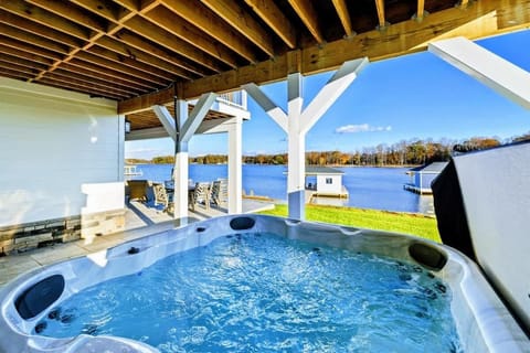 Covered patio featuring a relaxing hot tub with stunning views of the lake and nearby dock.
