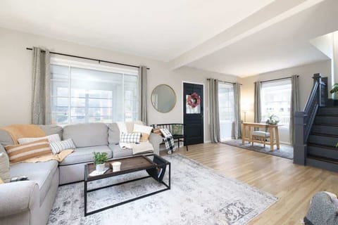Bright living room w/ comfy seating, TV & large windows filling the space w/ natural light