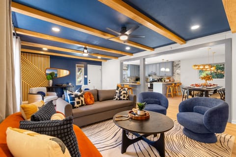 Stylish blue and wood accented ceilings add a touch of elegance to this open-concept living space. Bright and inviting living room with artistic decor and plush furniture.